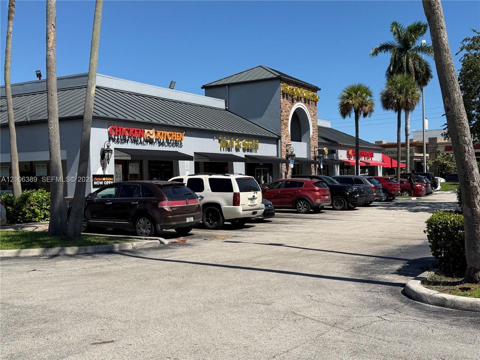 Commercial plaza exterior featuring a multi-tenant facade, metal roofing, stone masonry accents, and paved surface parking