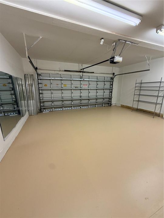 Attached garage featuring coated concrete flooring, a multi-panel overhead garage door, built-in metal shelving, and wall-mounted mirrors