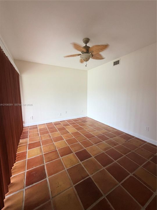 Interior room featuring square terra-cotta tile flooring, vaulted ceilings, and a ceiling fan with integrated light fixture