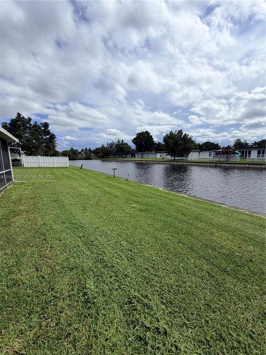 Waterfront lot featuring a grass lawn, white vinyl fencing, and direct canal frontage