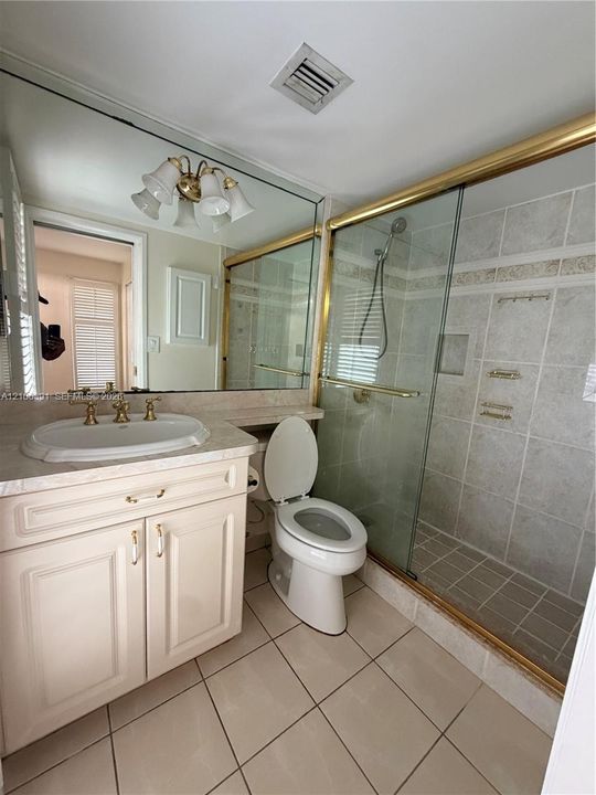 Bathroom featuring a vanity with integrated sink, brass-finish fixtures, full-width wall mirror, and a walk-in shower with glass enclosure
