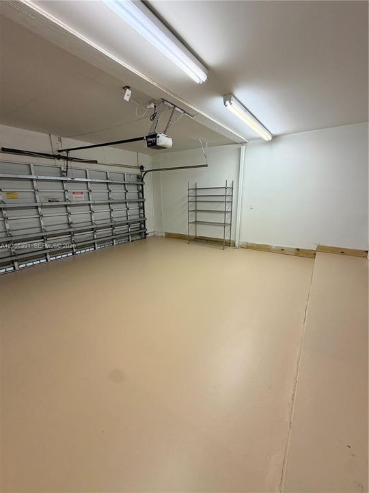 Finished garage interior featuring smooth-surface flooring, dual overhead fluorescent lighting, and an automated door opener mechanism