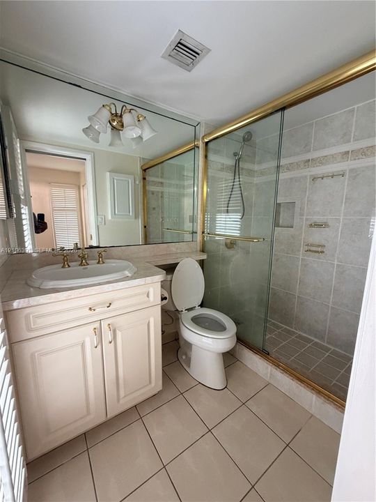 Bathroom featuring a single-sink vanity with stone countertop, tile-surround shower with glass enclosure, wall-to-wall mirror, and tile flooring