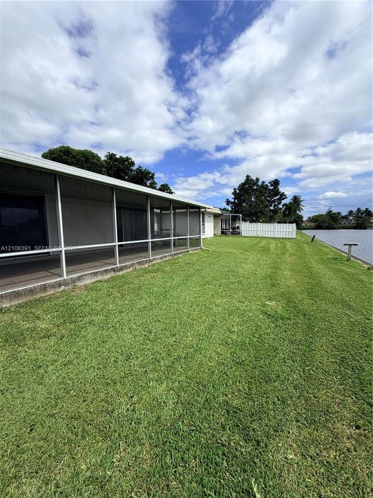 Screened-in rear porch featuring a concrete foundation, expansive lawn, white vinyl fencing, and direct water frontage