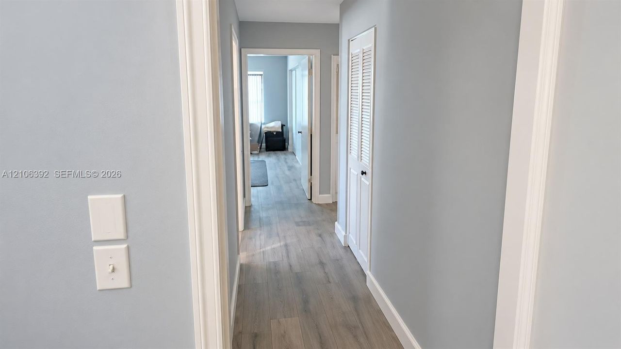 Hallway featuring wood-finish flooring, light-toned wall paint, and white louvered closet doors