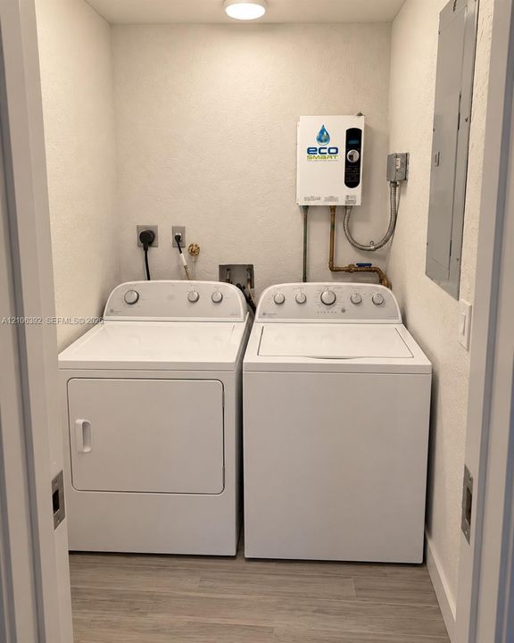 Utility closet featuring an electric tankless water heater, electrical service panel, laundry hookups, and wood-finish flooring