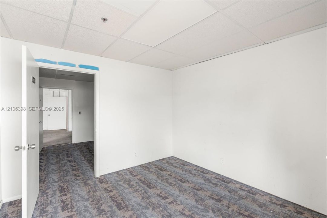 Interior room featuring white walls, patterned carpeted flooring, and a suspended drop ceiling