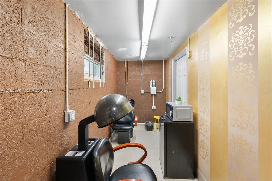 Utility area featuring painted masonry walls, decorative metallic-finish wall covering, linear fluorescent lighting, and tile flooring