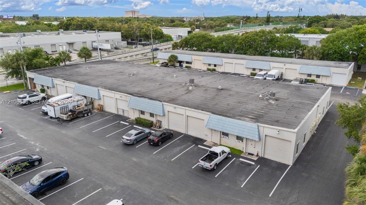 Industrial warehouse facility featuring multiple roll-up bay doors, dedicated surface parking, and blue metal awnings