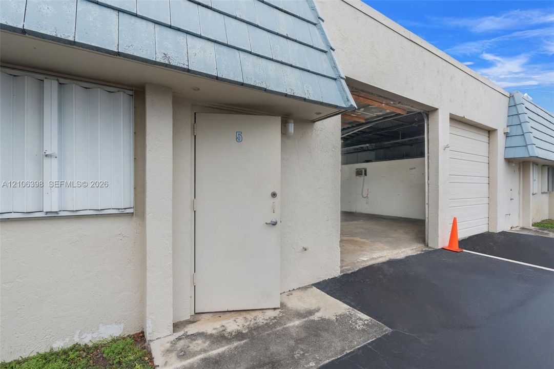 Exterior facade featuring a mansard roofline, textured stucco finish, a private entrance door, and an integrated garage space with a roll-up door