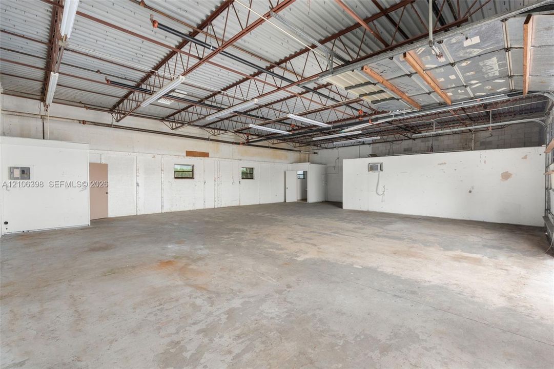 Expansive open-concept space featuring concrete flooring, high ceilings with exposed metal trusses, integrated fluorescent strip lighting, and white finished walls