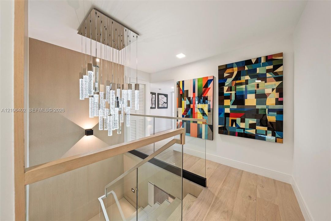 Multi-tiered crystal pendant light fixture, glass panel railing with wood handrail, and light-tone wood-finish flooring