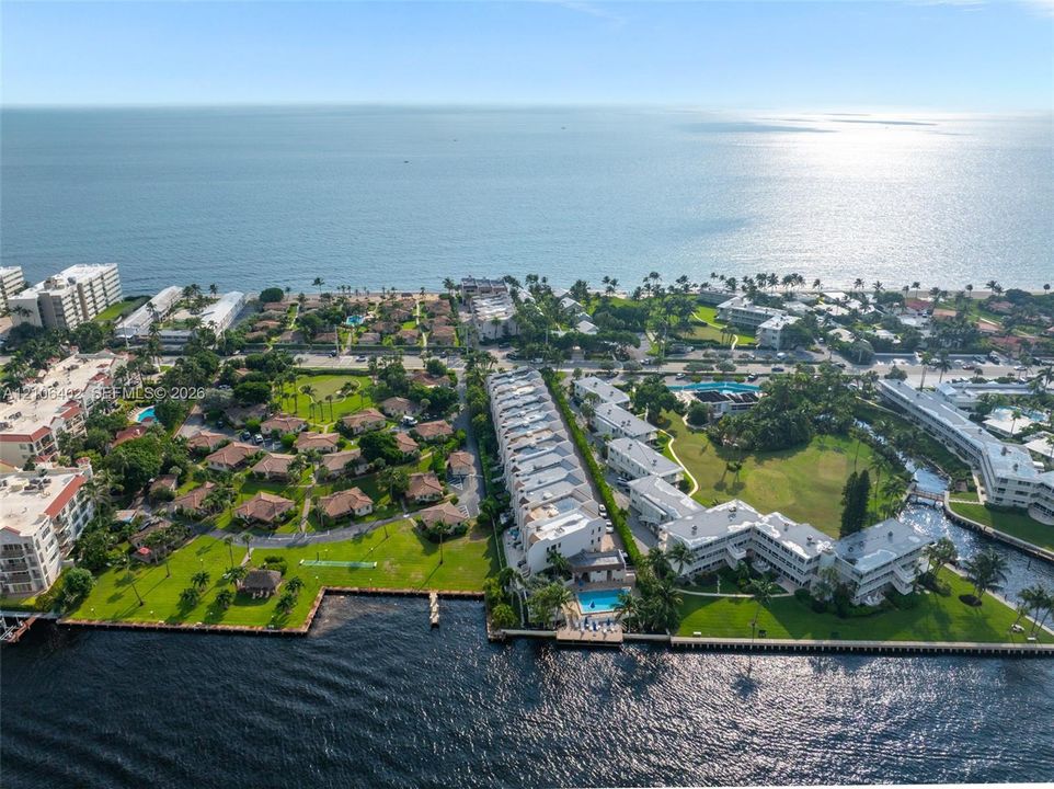 Aerial perspective of waterfront property featuring extensive manicured grounds, a private swimming pool, direct shoreline access, and mature palm landscaping