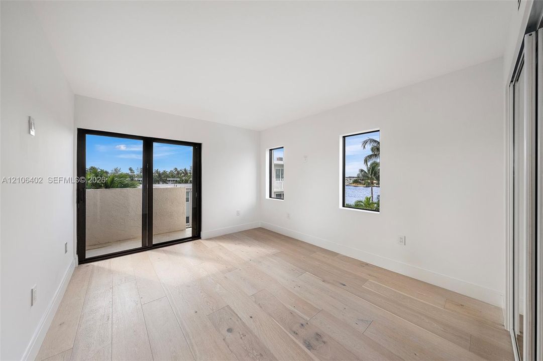 Wood-finish flooring, sliding glass door with black frame, two vertical windows, and built-in closet with mirrored doors