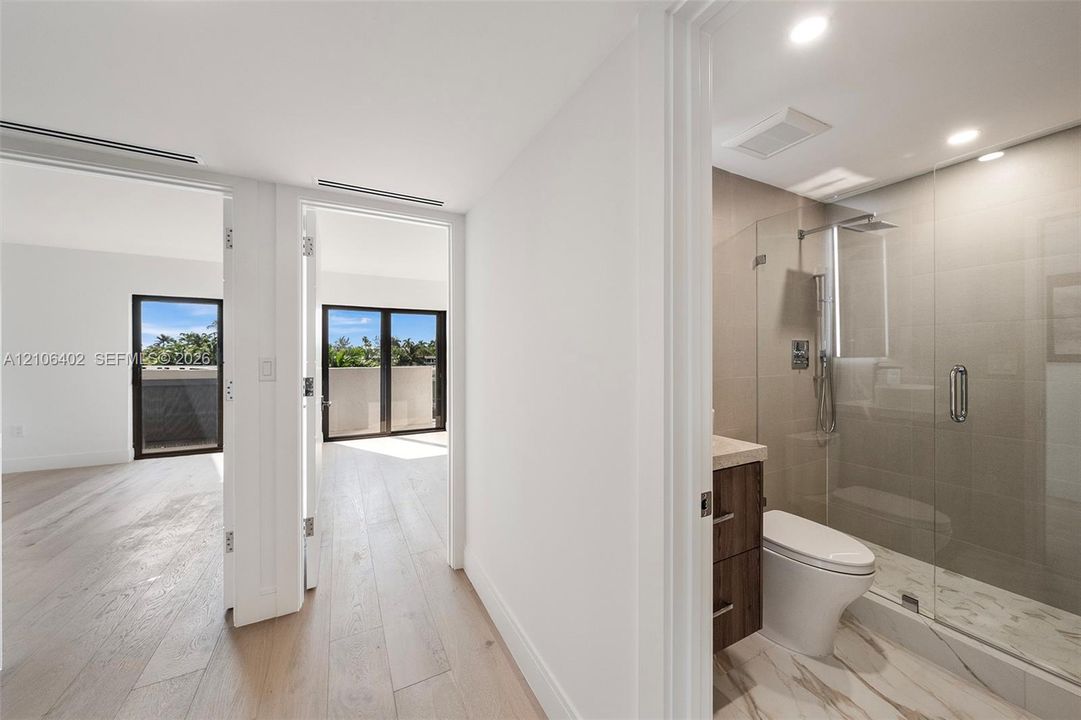 Bathroom featuring a frameless glass shower enclosure, wood-finish cabinetry, and neutral tile flooring; wood-finish flooring extending throughout the interior