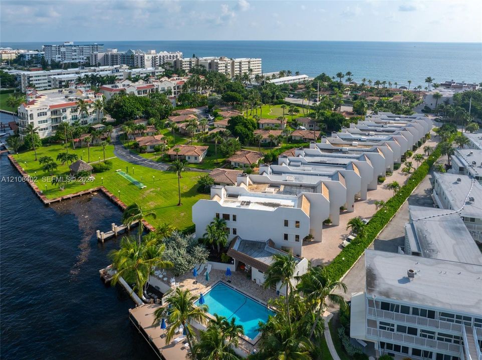 Aerial perspective featuring multi-story waterfront residential structures, an outdoor swimming pool, paved walkways, and expansive landscaped grounds