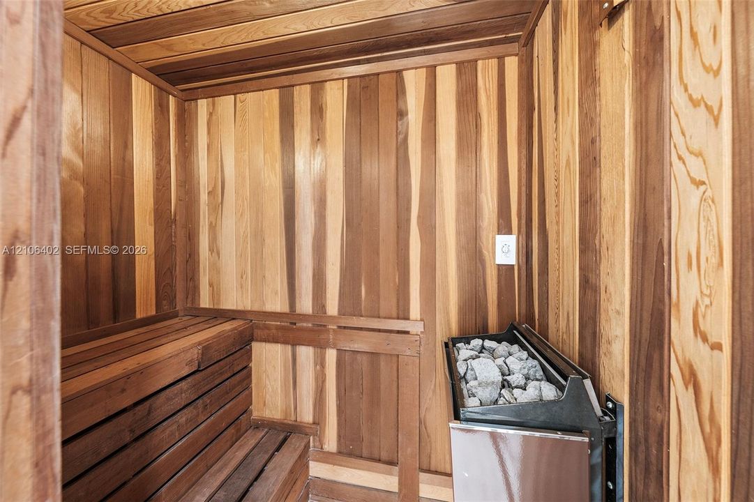 Sauna room featuring tongue-and-groove wood wall paneling, tiered wood bench seating, and an integrated heating element with stone fill