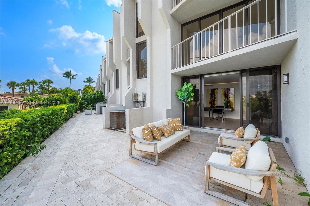 Ground-level stone paver patio featuring a herringbone pattern, integrated upper-level balcony, and full-height sliding glass doors
