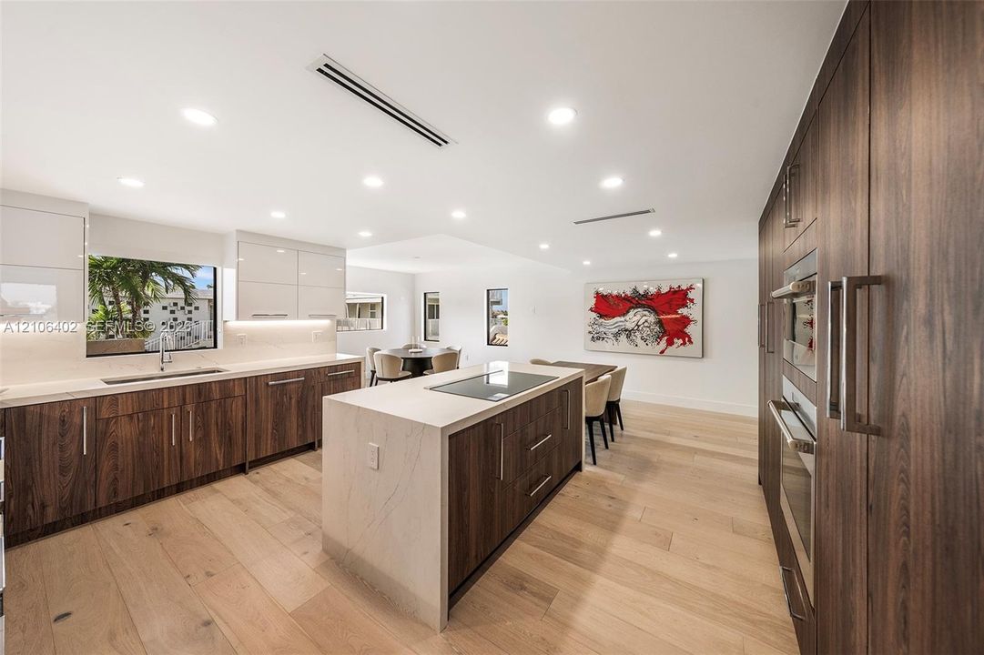 Kitchen featuring high-gloss upper cabinetry, wood-finish lower cabinetry, stone-surface countertops, center island with an integrated cooktop, and wide-plank wood-finish flooring