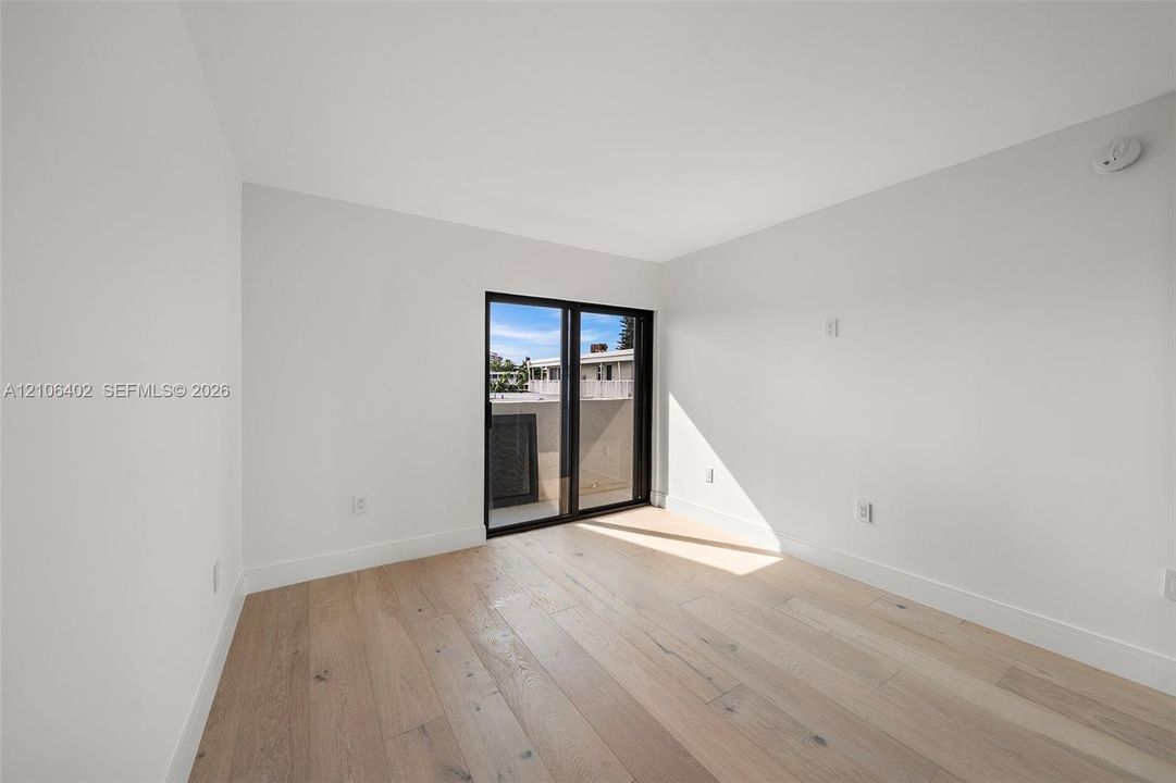 Neutral-toned interior featuring wood-finish flooring, white walls, and black-framed sliding glass doors opening to an exterior balcony