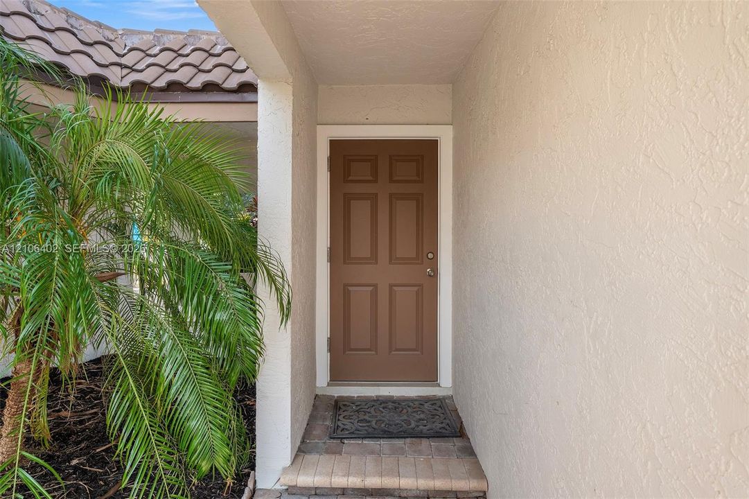 Covered entryway featuring a six-panel door, textured exterior stucco, and paver stone landing