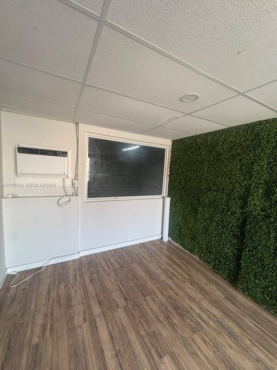 Room featuring wood-finish flooring, a textured green accent wall, dropped ceiling with recessed lighting, and a wall-mounted climate control unit