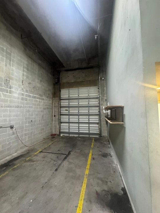 Industrial-style interior featuring concrete block walls, high ceilings, a sectional metal roll-up door, and concrete flooring