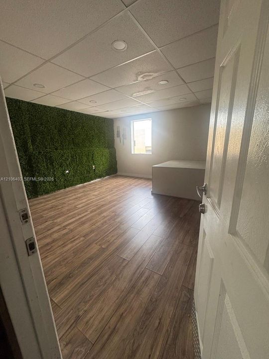 Room interior featuring wood-finish flooring, a textured artificial greenery accent wall, recessed lighting, and a drop ceiling
