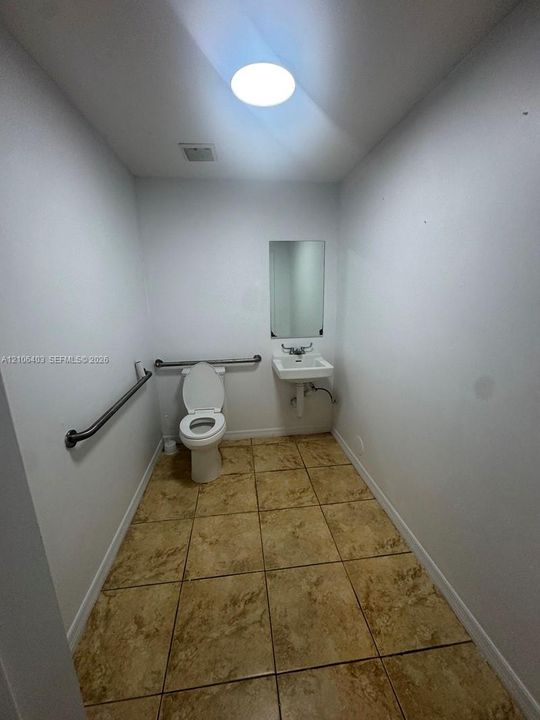 Restroom featuring ceramic tile flooring, a wall-mounted sink with dual-handle faucet, a rectangular mirror, and metal grab bars