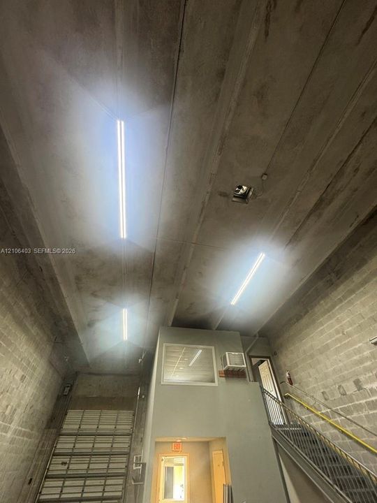 Industrial space featuring high ceilings with integrated linear lighting, concrete block walls, a metal staircase with handrails, and a sectional overhead door