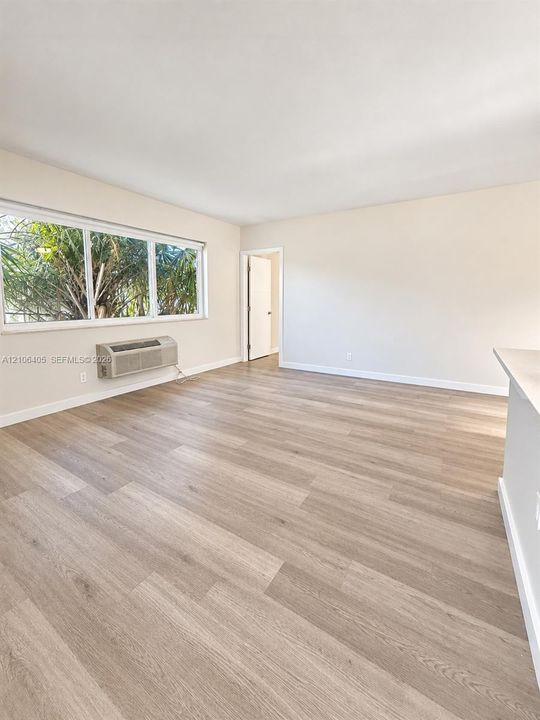 Neutral-toned living space featuring light wood-finish flooring, a large picture window, and a wall-mounted heating and cooling unit