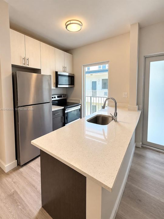 Kitchen featuring light-toned cabinetry, stainless steel appliances, quartz countertops, a stainless steel undermount sink with a gooseneck faucet, and wood-finish flooring