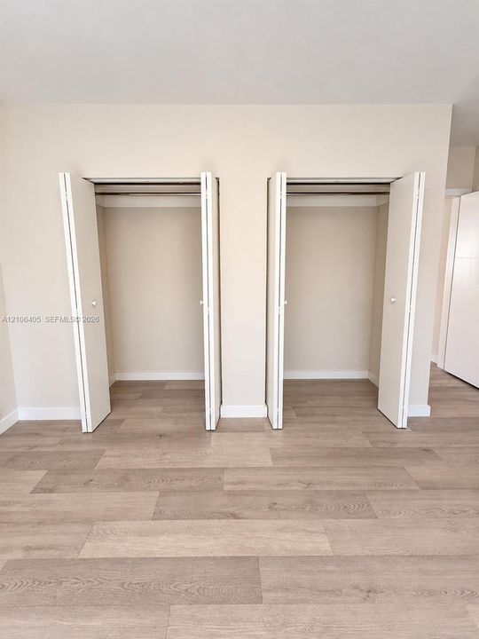 Dual reach-in closets featuring white bi-fold doors and wood-finish flooring