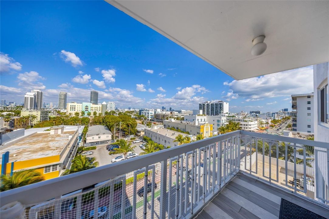 Covered balcony featuring wood-finish tile flooring and a white metal railing overlooking a cityscape