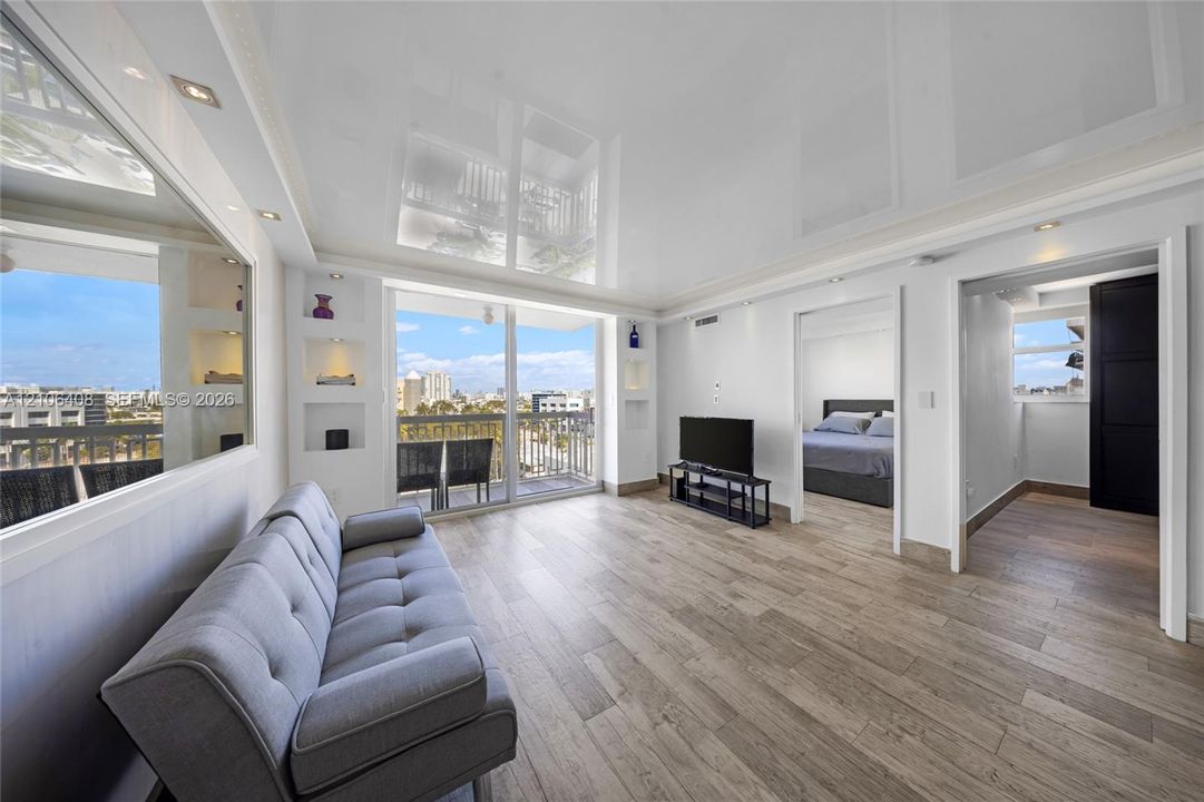 Living area featuring high-gloss reflective ceiling, wood-finish flooring, built-in display niches, and floor-to-ceiling glass sliding doors to the exterior
