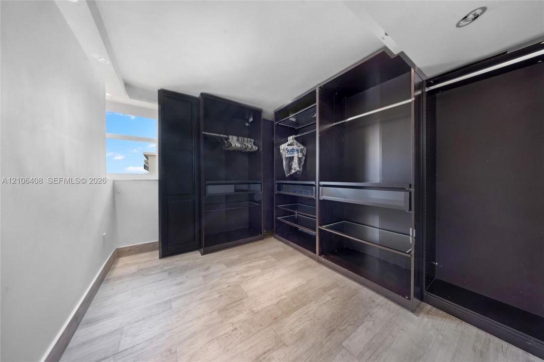 Custom floor-to-ceiling built-in cabinetry featuring dark finish shelving, pull-out drawers, and hanging rods, paired with wood-finish flooring and recessed lighting