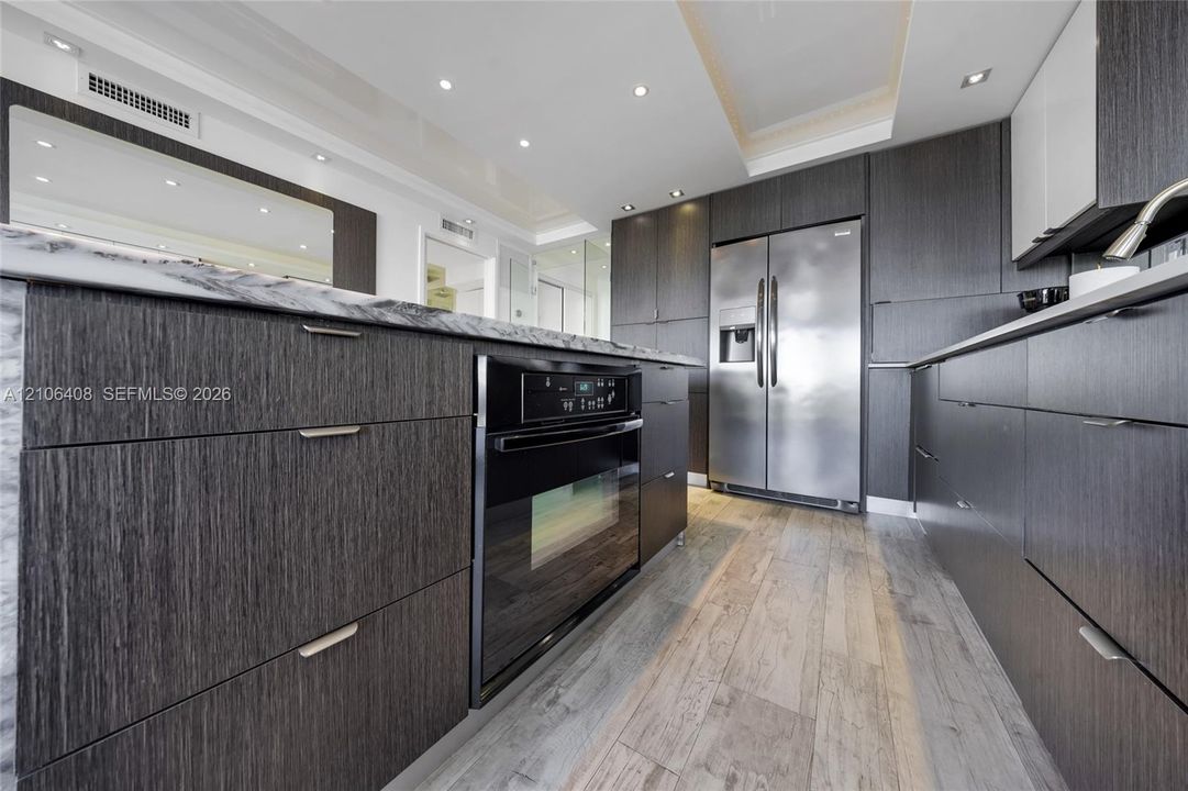 Kitchen featuring textured dark cabinetry, stone-finish countertops, stainless steel side-by-side refrigerator, built-in oven, and wood-finish flooring