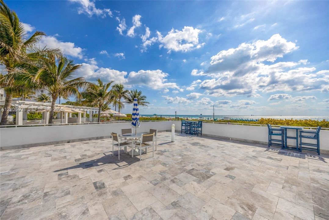 Expansive stone-tiled terrace featuring a perimeter wall, metal railing, and mature palm trees
