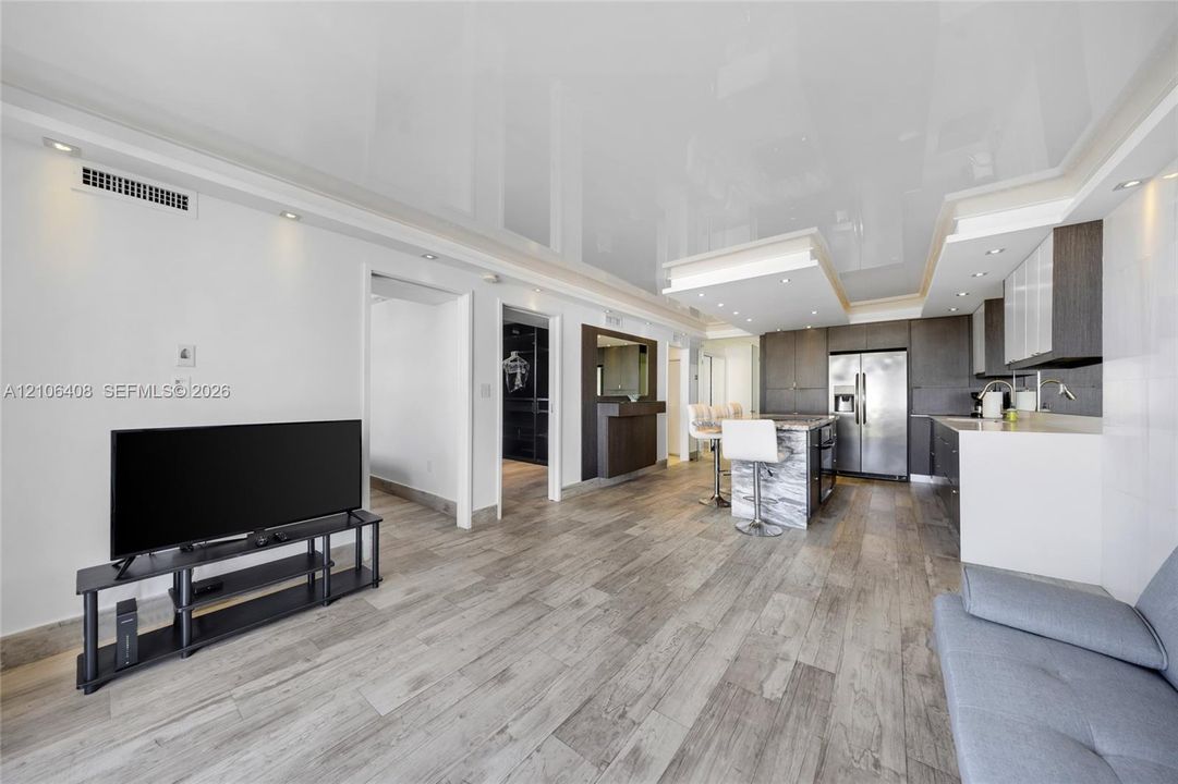 Open-concept space featuring a high-gloss ceiling, wood-finish flooring, recessed lighting, built-in cabinetry, and a kitchen island with a stone-finish facade