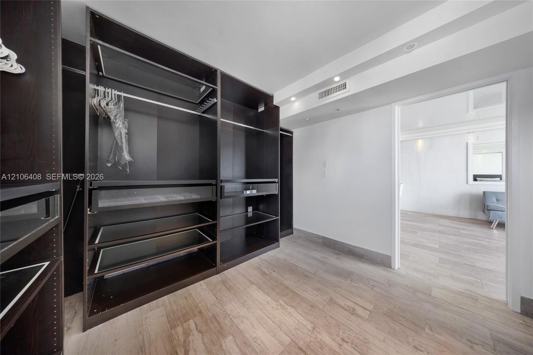 Walk-in closet featuring custom dark-finish floor-to-ceiling cabinetry, integrated shelving units, recessed ceiling lighting, and wood-finish flooring
