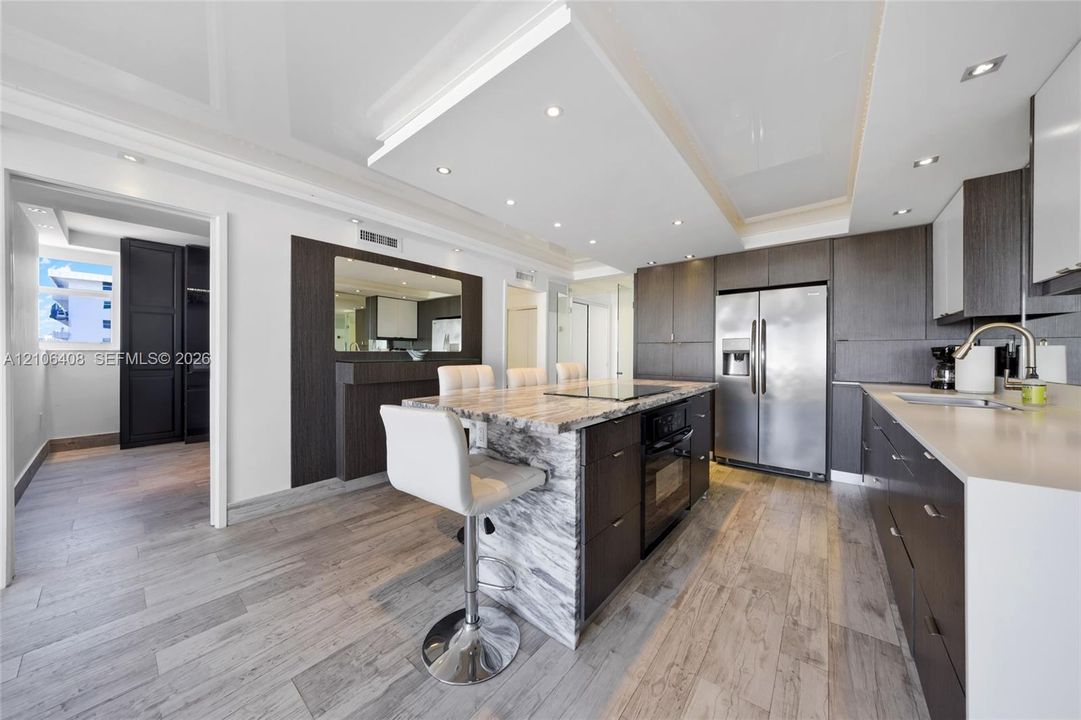 Kitchen featuring high-gloss cabinetry, stone-topped island with integrated cooktop, wood-finish flooring, and recessed ceiling lighting