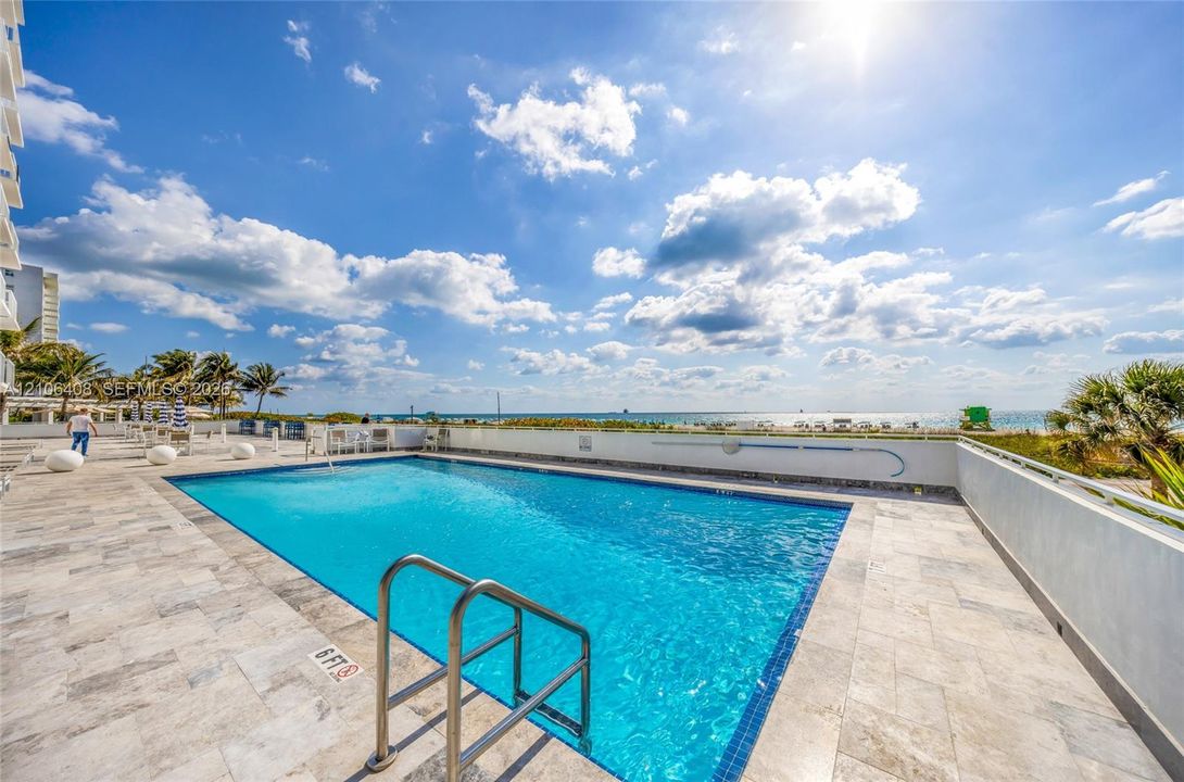 Swimming pool featuring stone-finish decking, stainless steel ladder, and metal perimeter railing