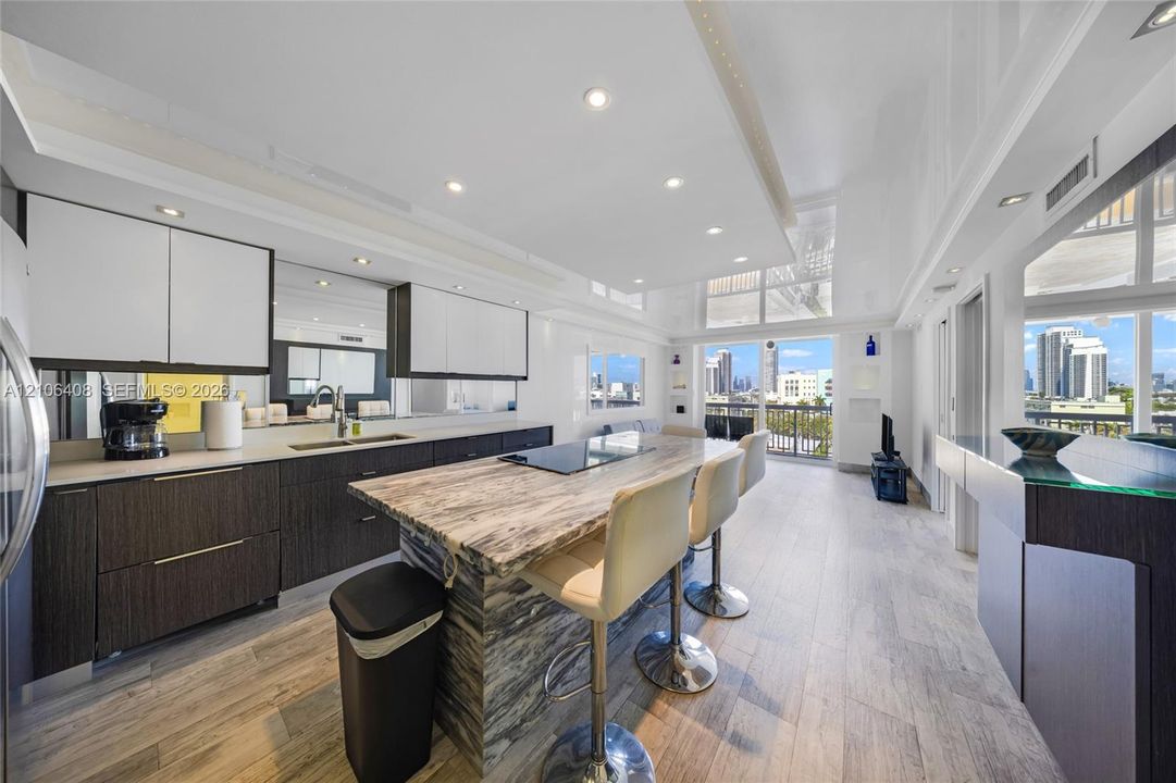 Modern kitchen featuring high-contrast cabinetry, a stone-finish waterfall island, recessed lighting, and wood-finish flooring