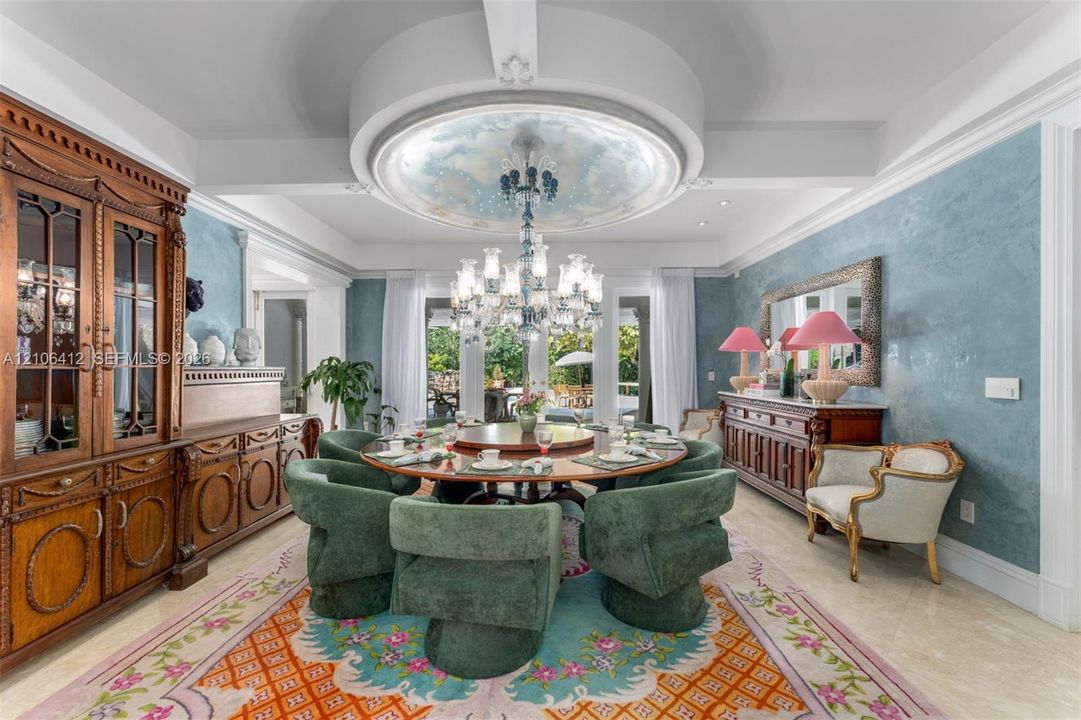 Formal dining room featuring a coffered ceiling with a recessed circular architectural detail, decorative wall finishes, built-in wooden cabinetry, a multi-tiered crystal chandelier, and glass-paned double doors
