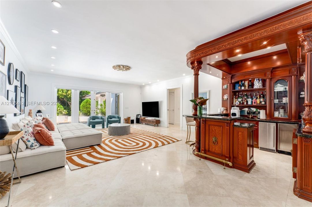 Custom built-in wet bar with wood cabinetry and decorative corbels, stone flooring, recessed lighting, and double glass doors