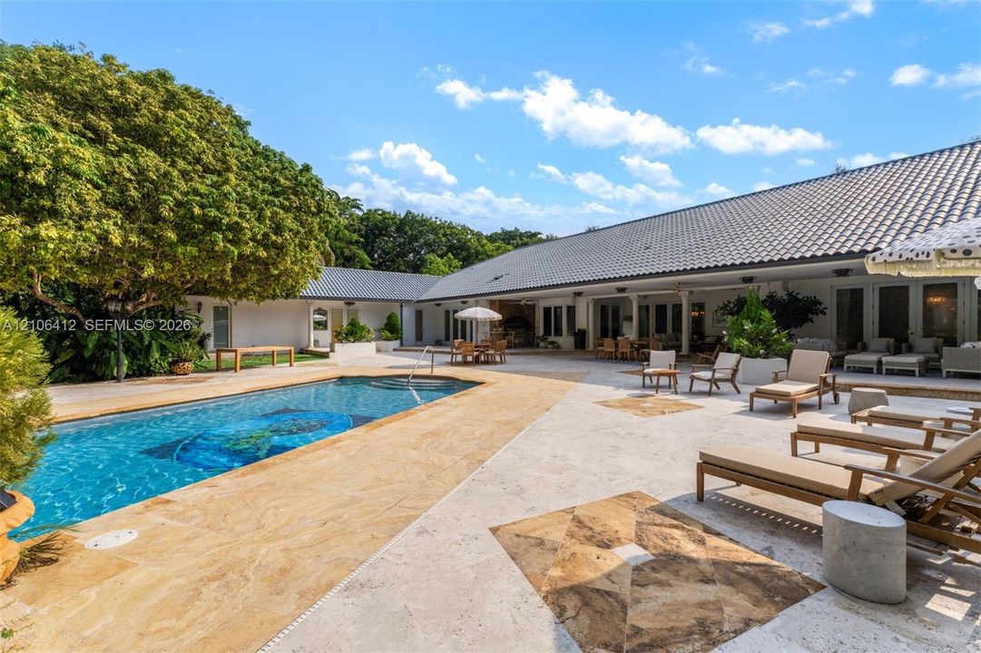 Outdoor living space featuring an expansive stone patio, an in-ground swimming pool with built-in stairs, a covered loggia, and mature landscaping