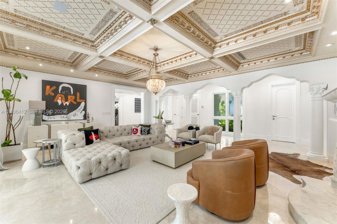 Coffered ceiling featuring intricate gold-leaf detailing, polished stone flooring, custom arched architectural columns, recessed lighting, and ornate hanging pendant light fixture