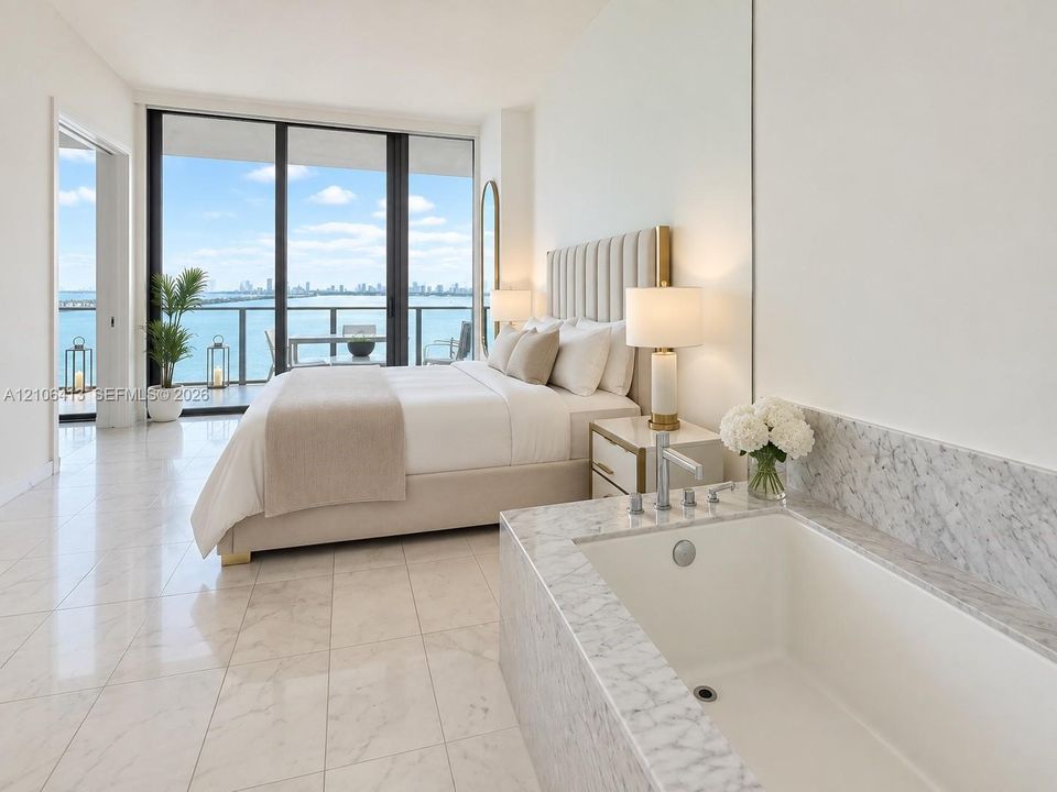 Floor-to-ceiling glass sliding doors, stone tile flooring, built-in soaking tub with stone surround, and balcony with metal railing