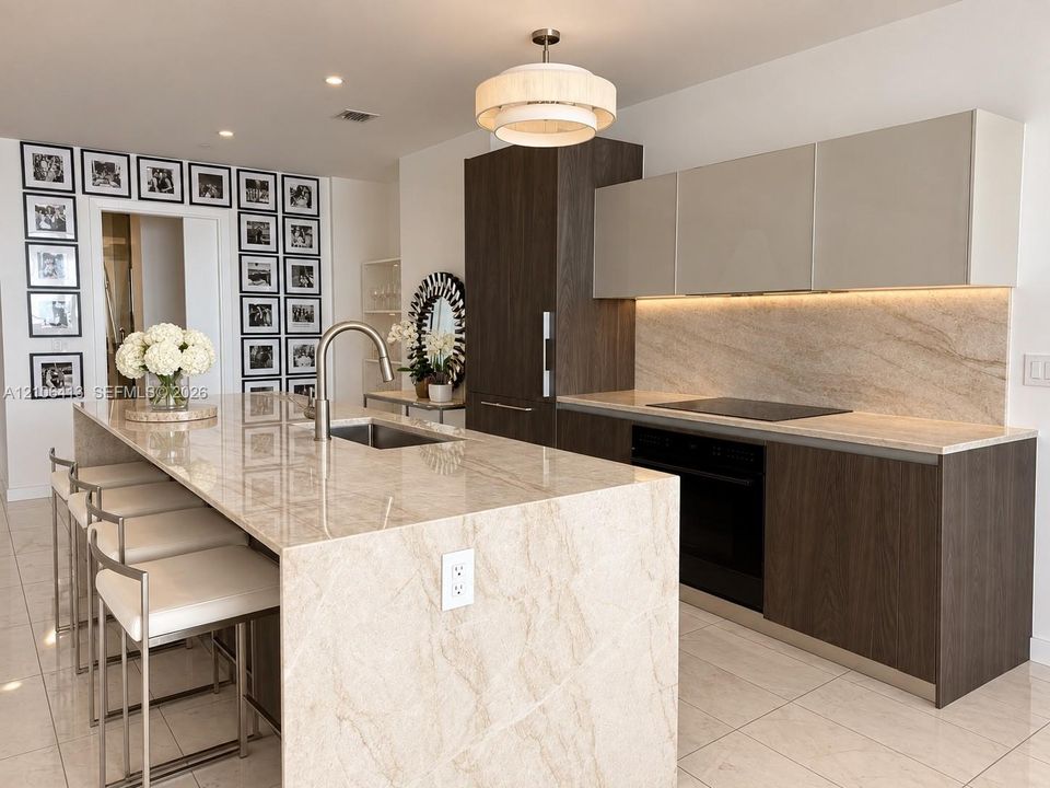 Kitchen featuring a stone-topped island with an integrated sink, custom two-tone cabinetry, recessed under-cabinet lighting, a built-in induction cooktop, and polished tile flooring