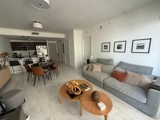 Open-concept interior featuring large-format stone-finish tile flooring, kitchen with dark wood-finish cabinetry, quartz countertops, integrated stainless steel appliances, and ceiling-mounted flush lighting fixtures